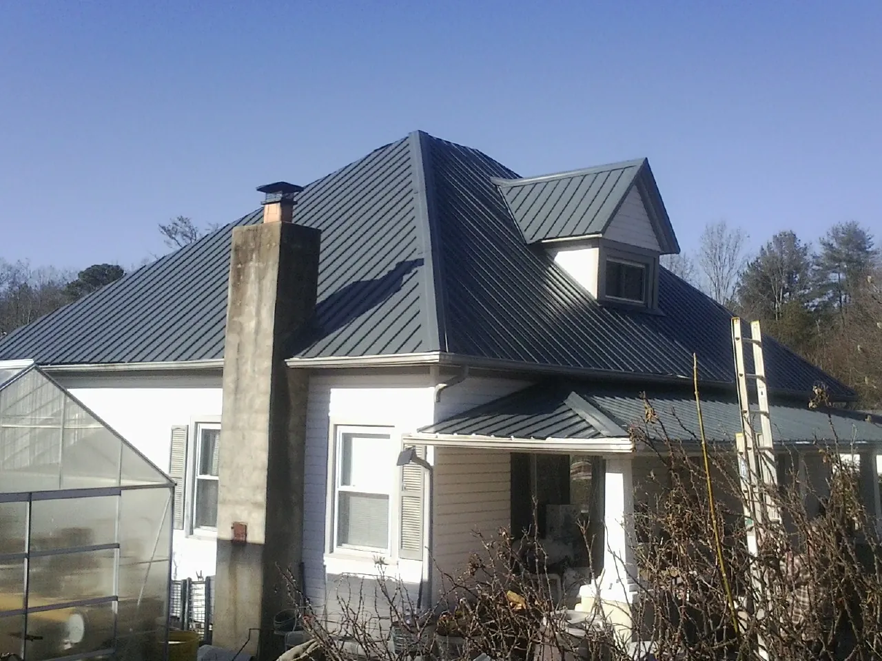 Dark blue standing seam metal roof on a white farmhouse with dormer — Slate & Tile Roof Repair by Roofing Brothers in Big Bear City
