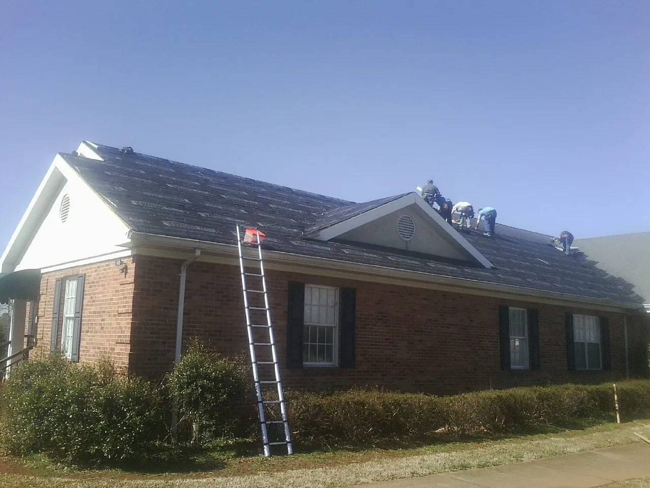 Crew tearing shingles off a brick ranch roof with a ladder set — Emergency Roof Repair work by our crew in Big Bear City