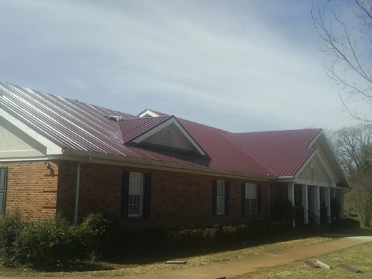 Red metal roof with gabled entries on a long brick building, from a Hail Damage Roof Repair job in Big Bear City