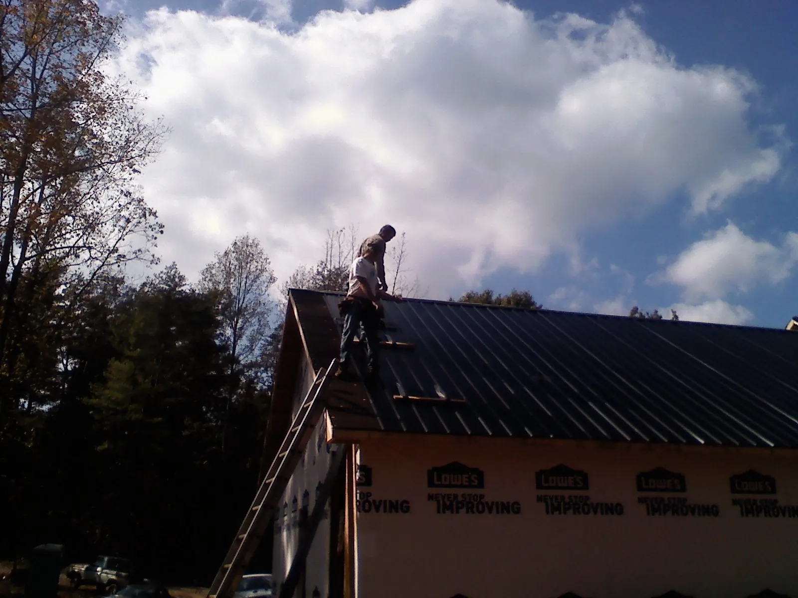 Roofer fastening dark metal panels high against a cloudy sky, from a Roof Inspection job in Big Bear City