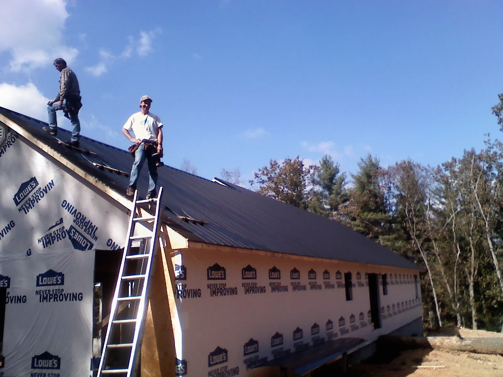 Two roofers standing on a long dark metal roof over a wrapped building in Big Bear City