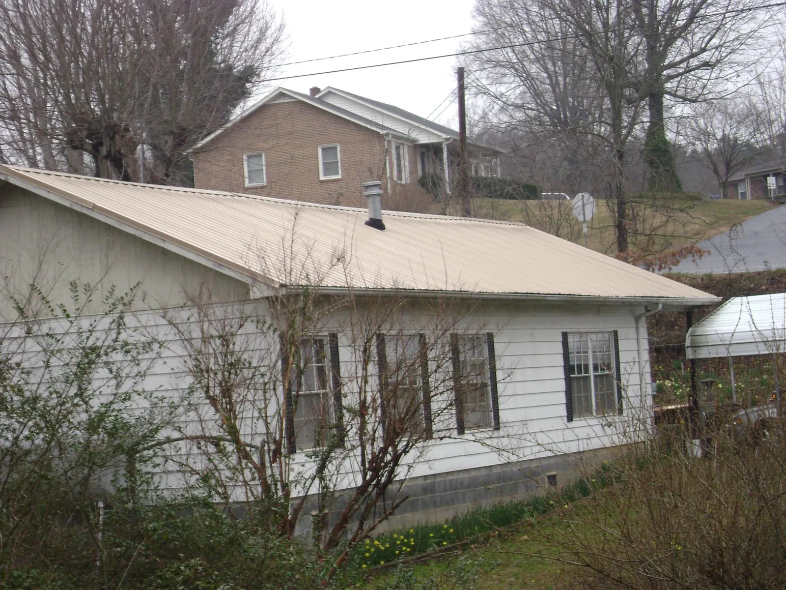 Tan metal roof on a white sided house set into a hillside — Commercial Roofing by Roofing Brothers in Big Bear City